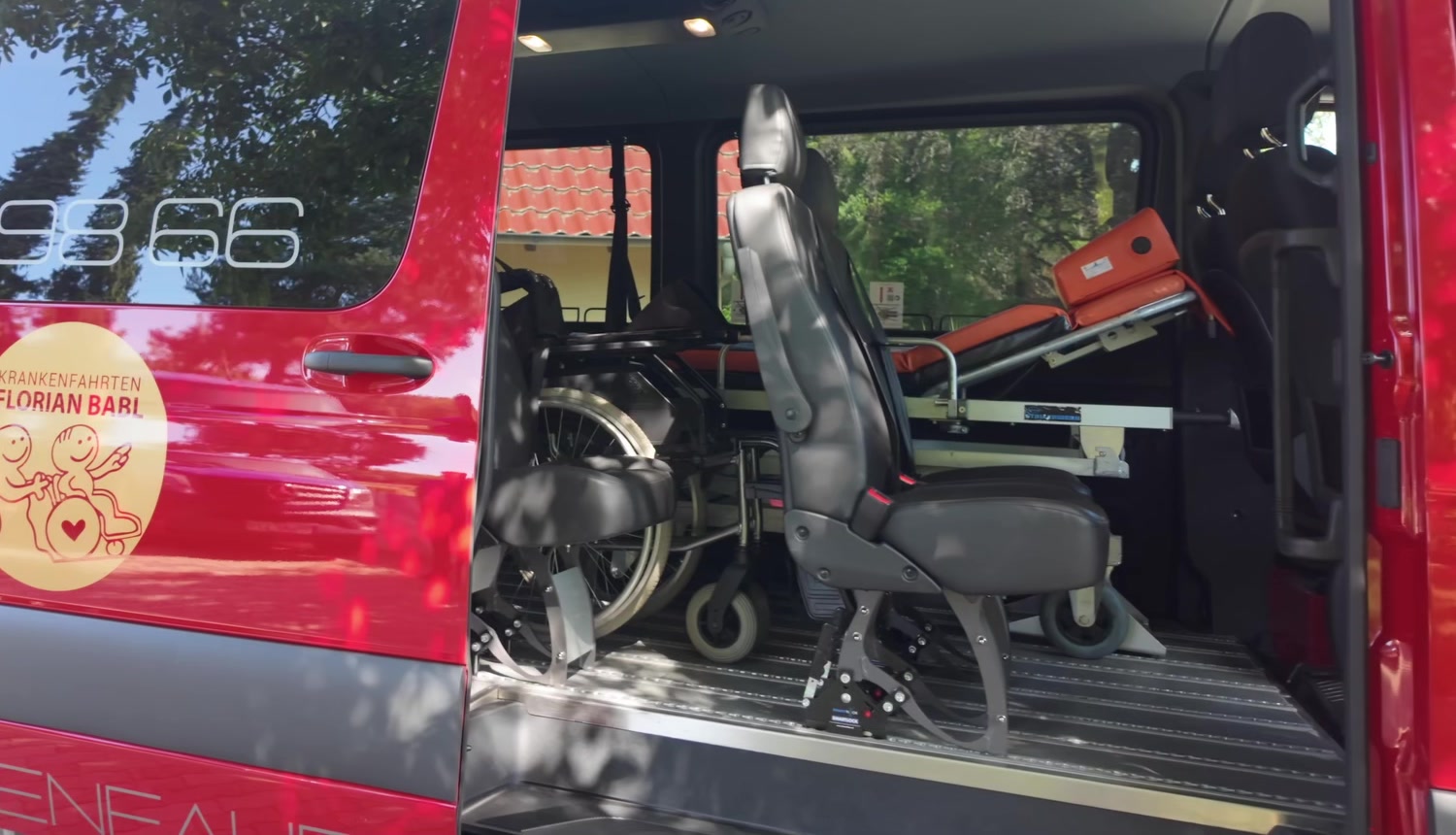 Rotes Krankenfahrten-Fahrzeug mit geöffneter Schiebetür, Blick auf Rollstuhlplatz und Trage
